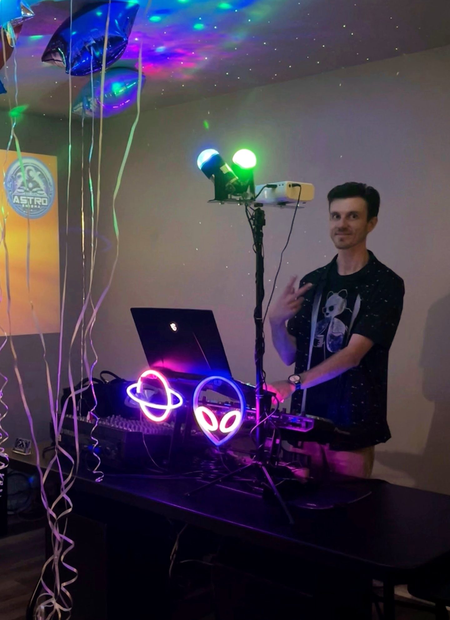 Astro Enigma behind the DJ booth under colorful party lighting